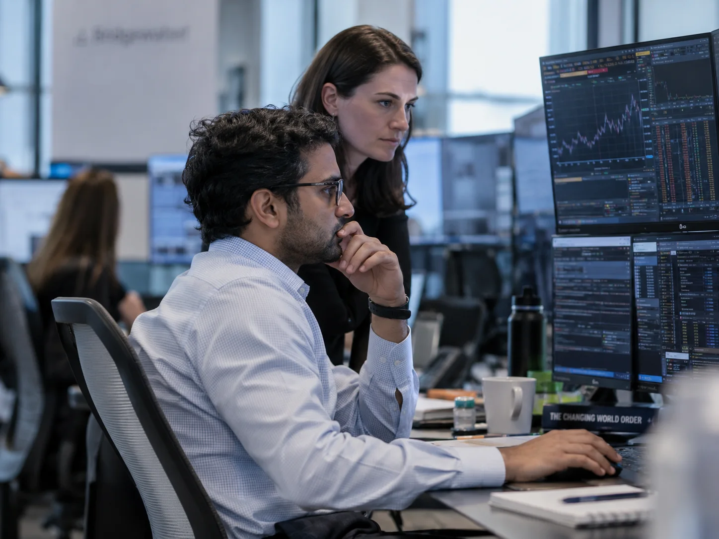 Two people looking at charts and tables on monitors at a workstation.